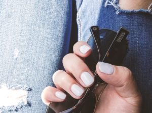 gift for mom manicure white gel nails hand holding coach sunglasses against blue jeans