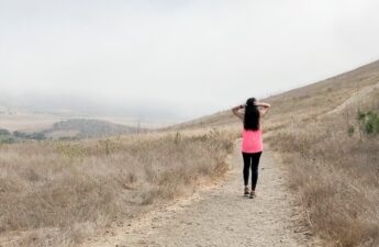 girl walking down a hiking trail wearing bright pink top and black pants
