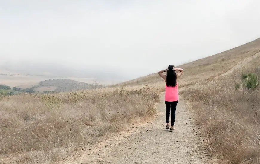 girl walking down a hiking trail wearing bright pink top and black pants